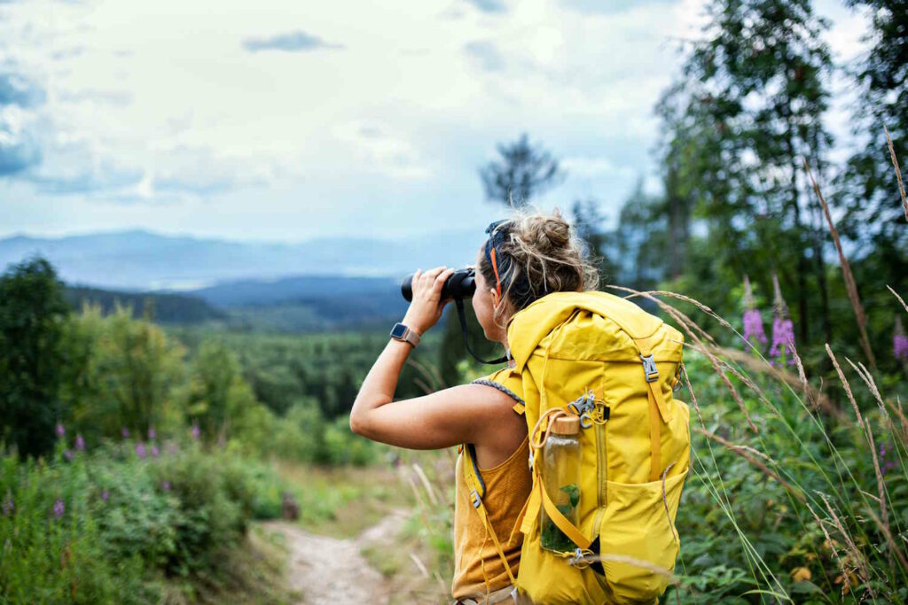 Frau auf Wanderung schaut durch ein Fernglas und bewundert die Natur.