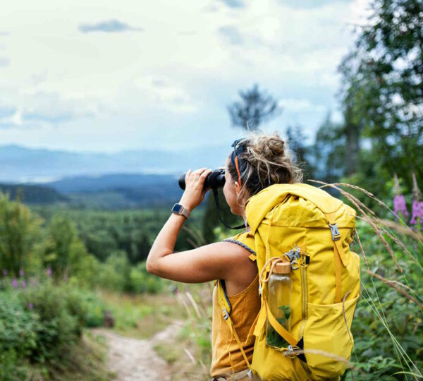 Frau auf Wanderung schaut durch ein Fernglas und bewundert die Natur.