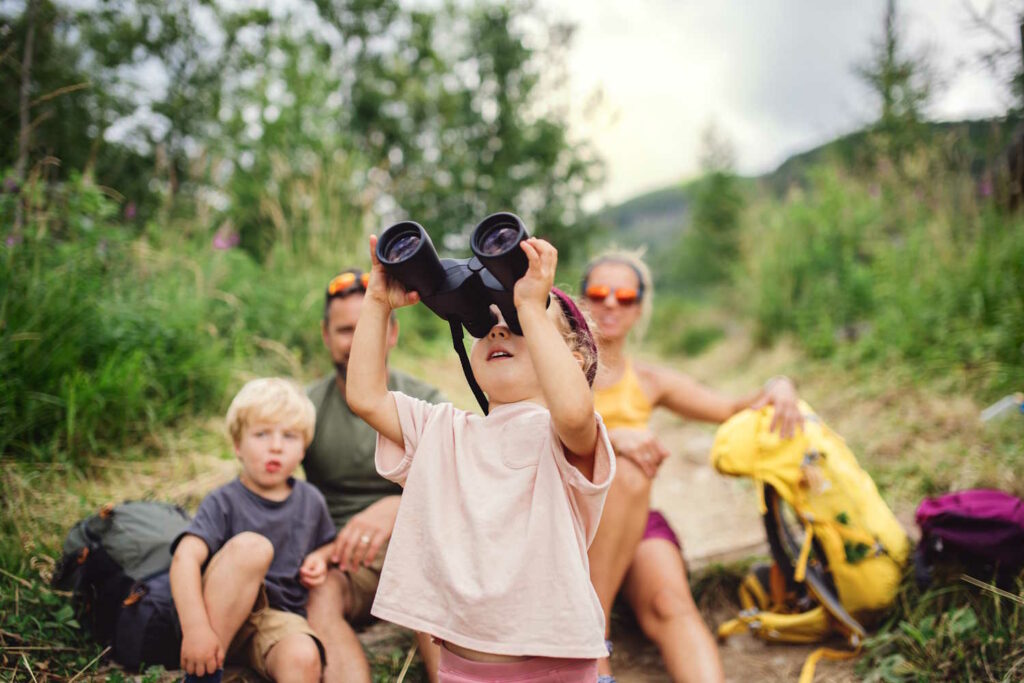 Familie beim Wandern mit Kinder, dass durch ein Fernglas schaut.